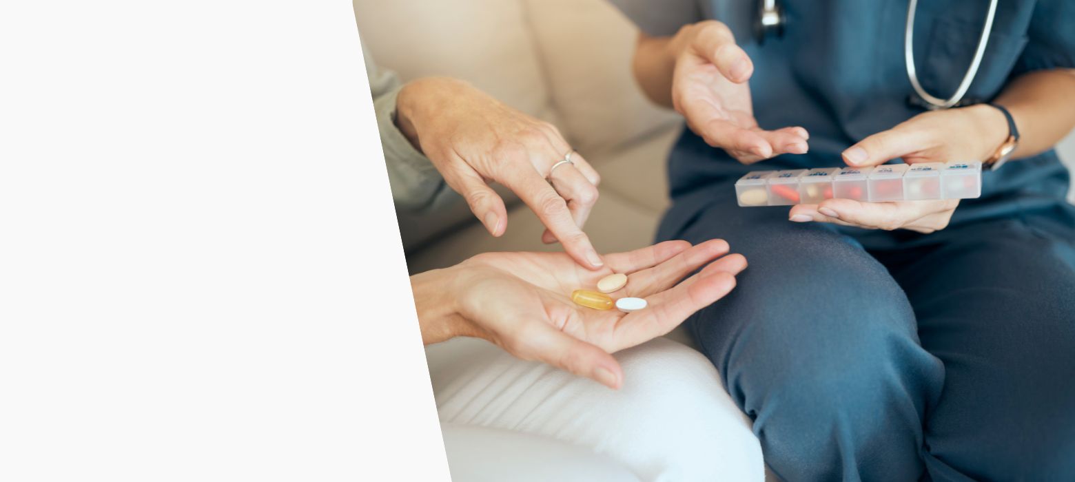 Eine ältere Frau hält mehrere Medikamnete in der Hand und eine Apothekerin zeigt mit Ihrer Hand auf eine Medikamnetenbox